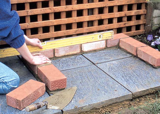 Guide to assembling a brick BBQ with a chimney, layering the first brick